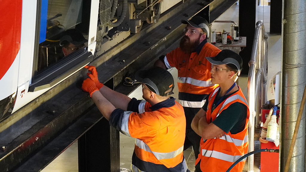 2 Maintenance team members working on a tram with a workplace learning student watching